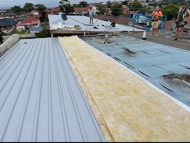 A Group Of People Are Working On The Roof Of A Building — Elevated Roofing Systems Pty Ltd In Barrack Heights, NSW