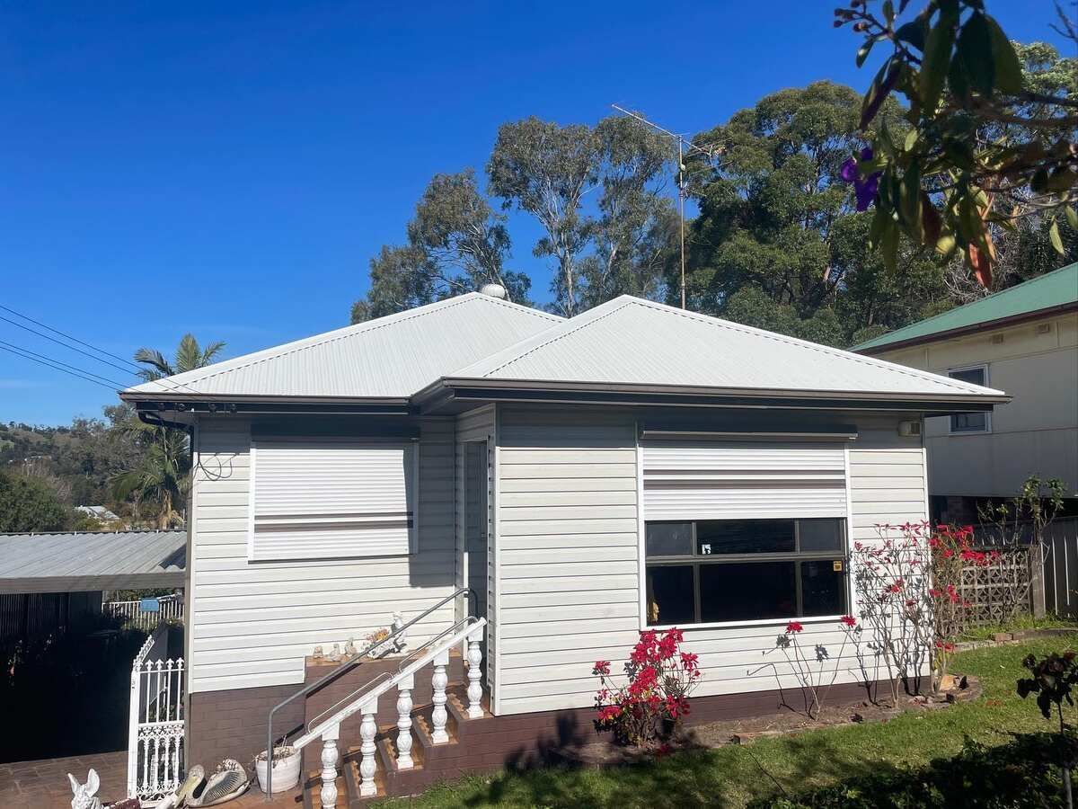 A Small White House With A White Roof Is Sitting On Top Of A Hill — Elevated Roofing Systems Pty Ltd In Barrack Heights, NSW