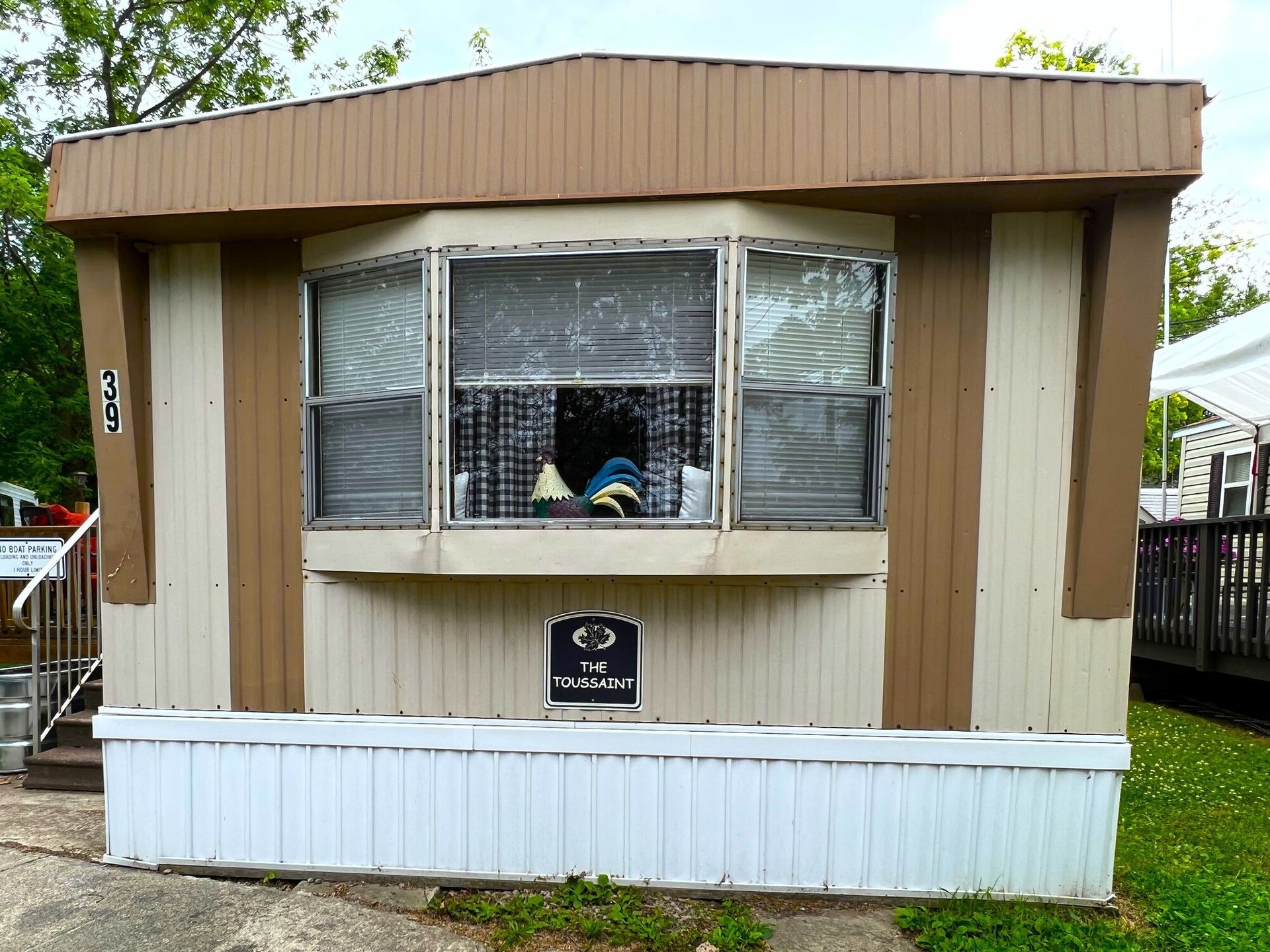 Small tan and brown mobile office with a front window and white skirting, set outdoors among trees.