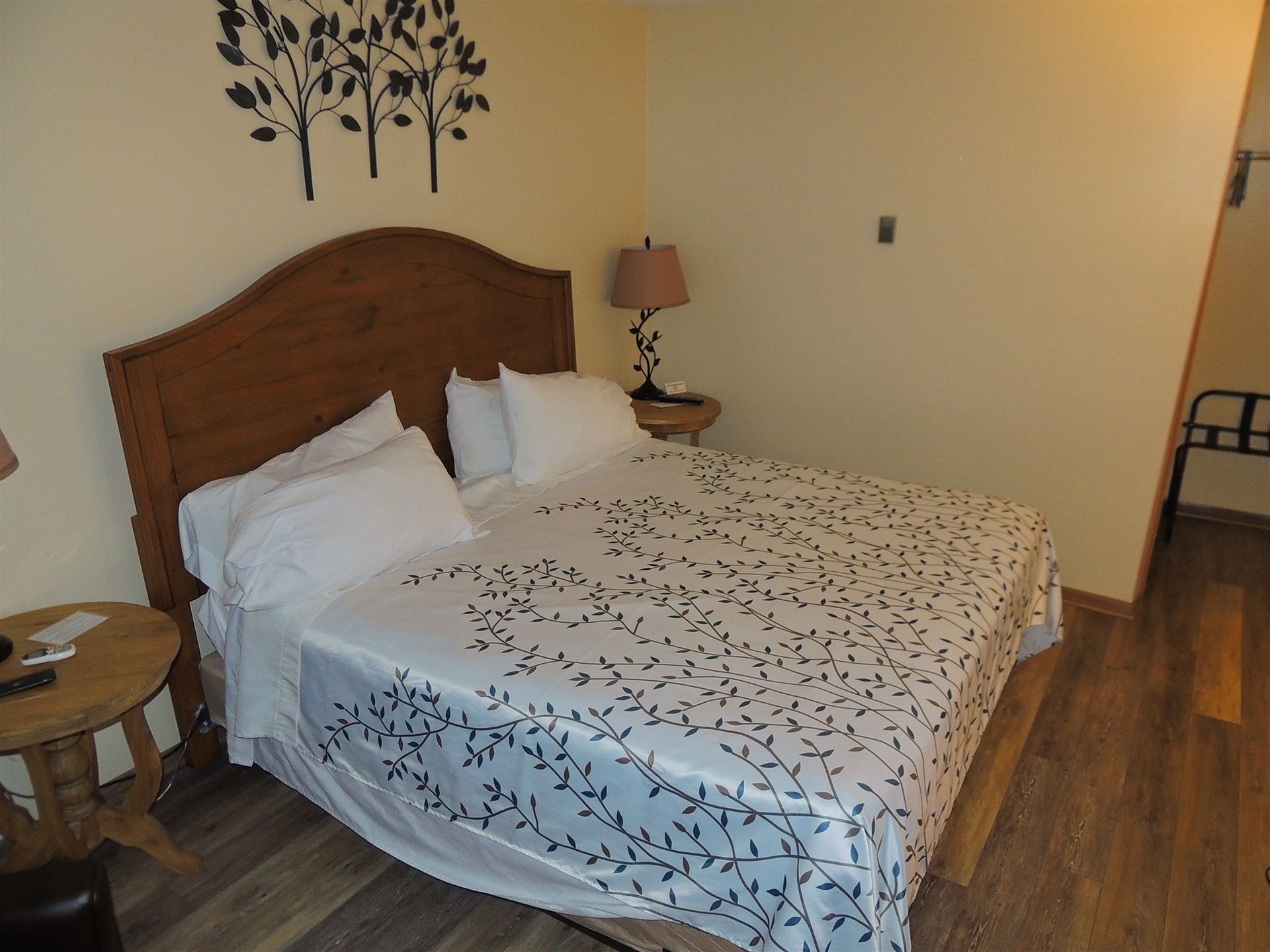 Cozy bedroom with a wooden bed, white patterned bedding, bedside table, and wall decor