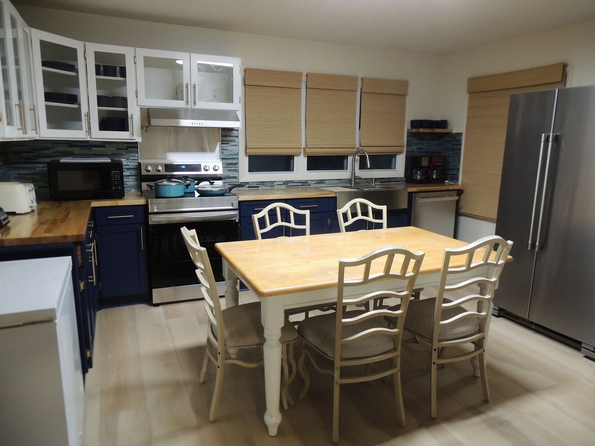 Kitchen with white cabinets, wood dining table, and stainless steel refrigerator on beige tile floor