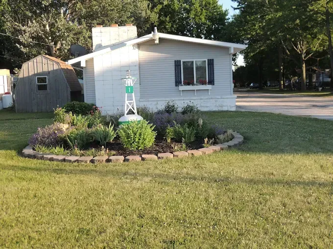 Small white house with a landscaped front yard and stone flower bed on a grassy lot