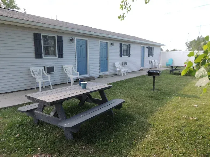 Backyard picnic table and grill beside a white house with blue doors and chairs on the porch