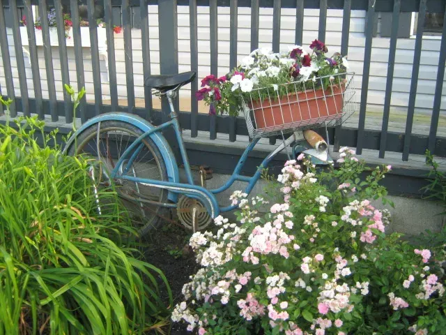 Blue bicycle with flower baskets parked beside a fence and garden greenery.