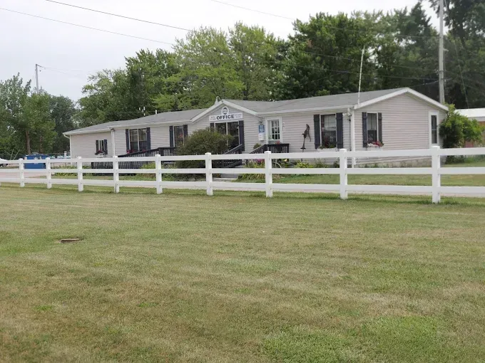 Single-story beige house with a white fence on a grassy lot under an overcast sky