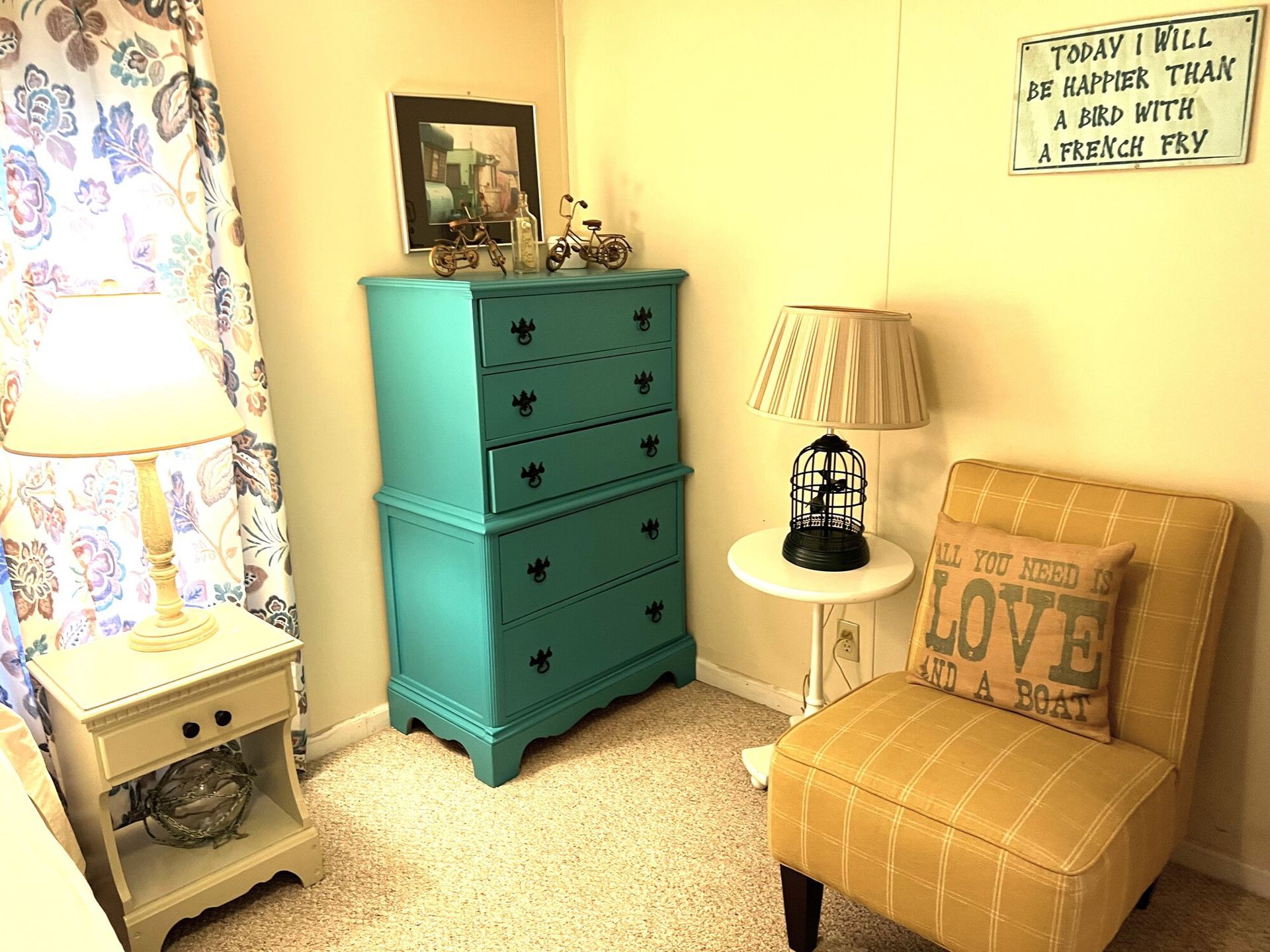 Cozy bedroom corner with teal dresser, tan chair, lamp, and floral curtains