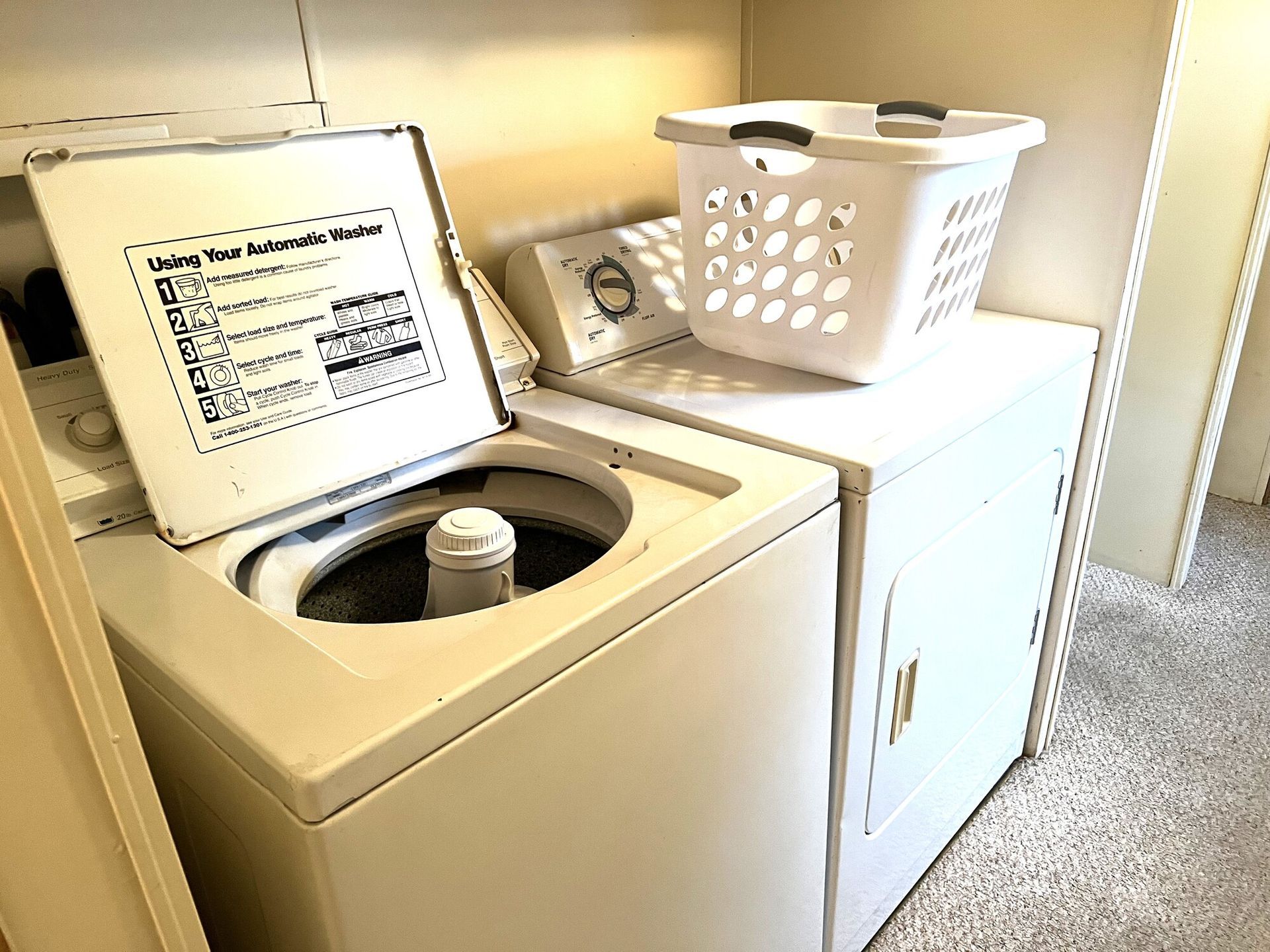 Laundry room with washer and dryer; washer lid open and laundry basket on top of dryer.