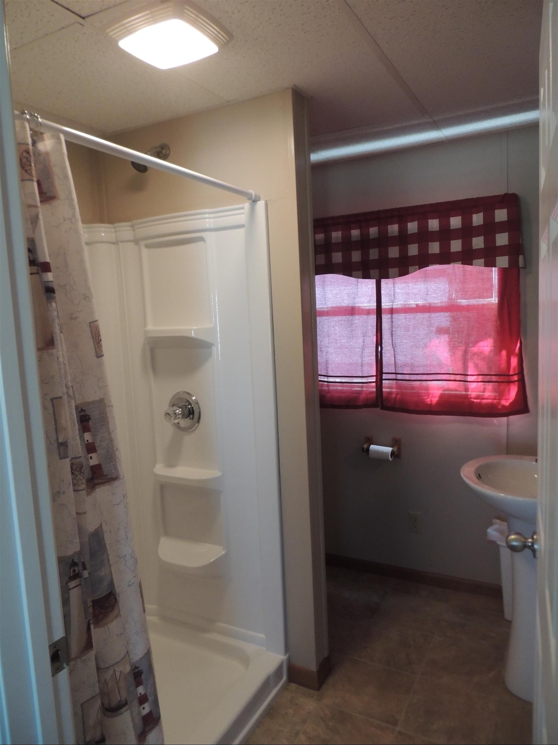 Bathroom with walk-in shower, toilet, sink, and a window covered by red blinds.
