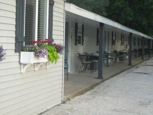 Covered porch with gray siding, chairs, and hanging flower planters beside a gravel driveway