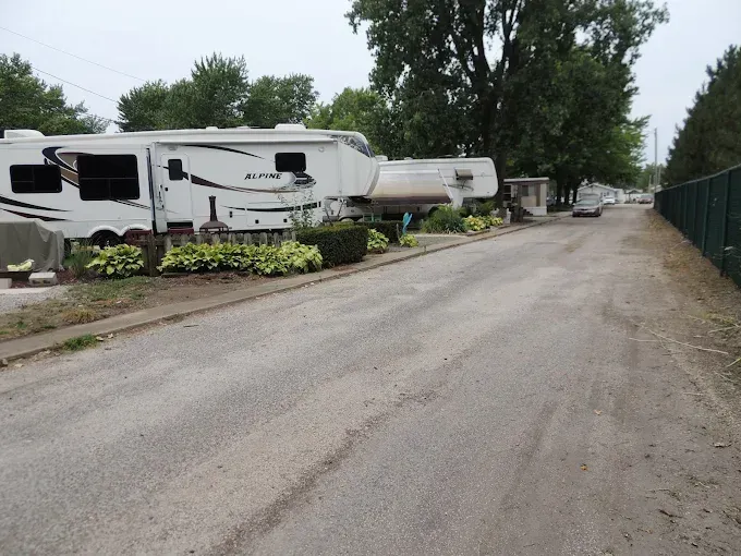 Row of parked RVs beside a gravel road under trees on an overcast day