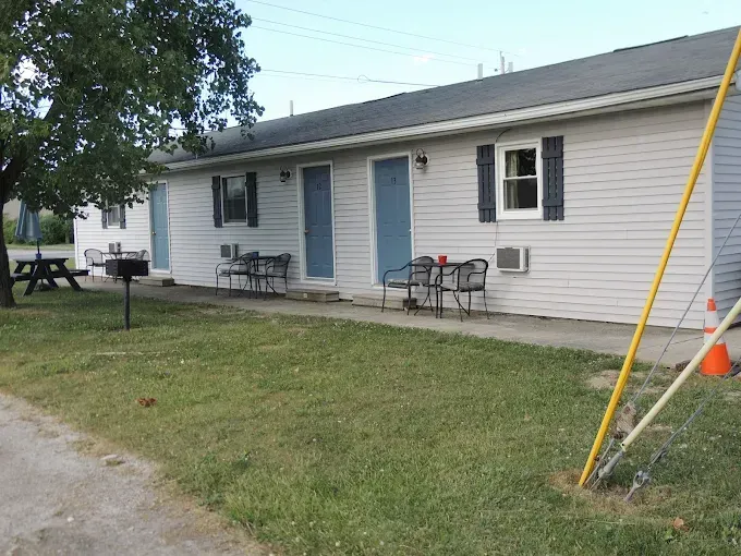 Single-story white house with blue doors and windows, small front porch, chairs, and a grassy yard
