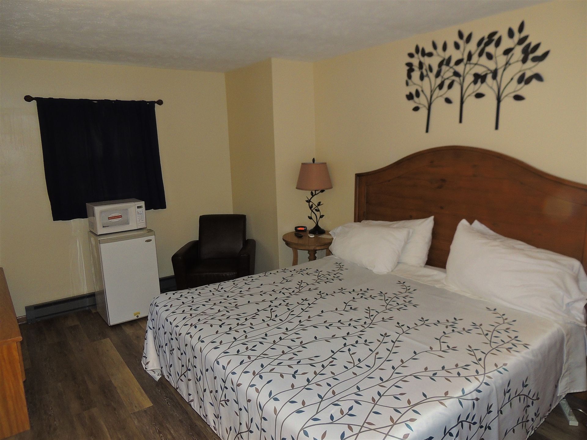 Bedroom with a bed, patterned comforter, window, chair, nightstand, and wall tree decal