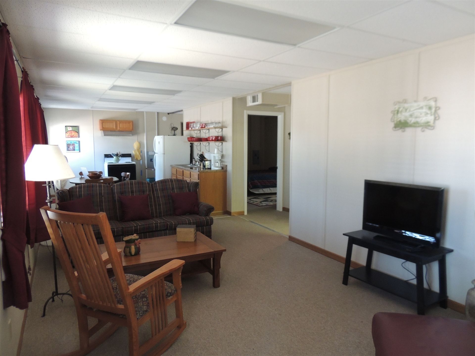 Living room with wooden chairs, TV on a stand, and an open view into a kitchen area.