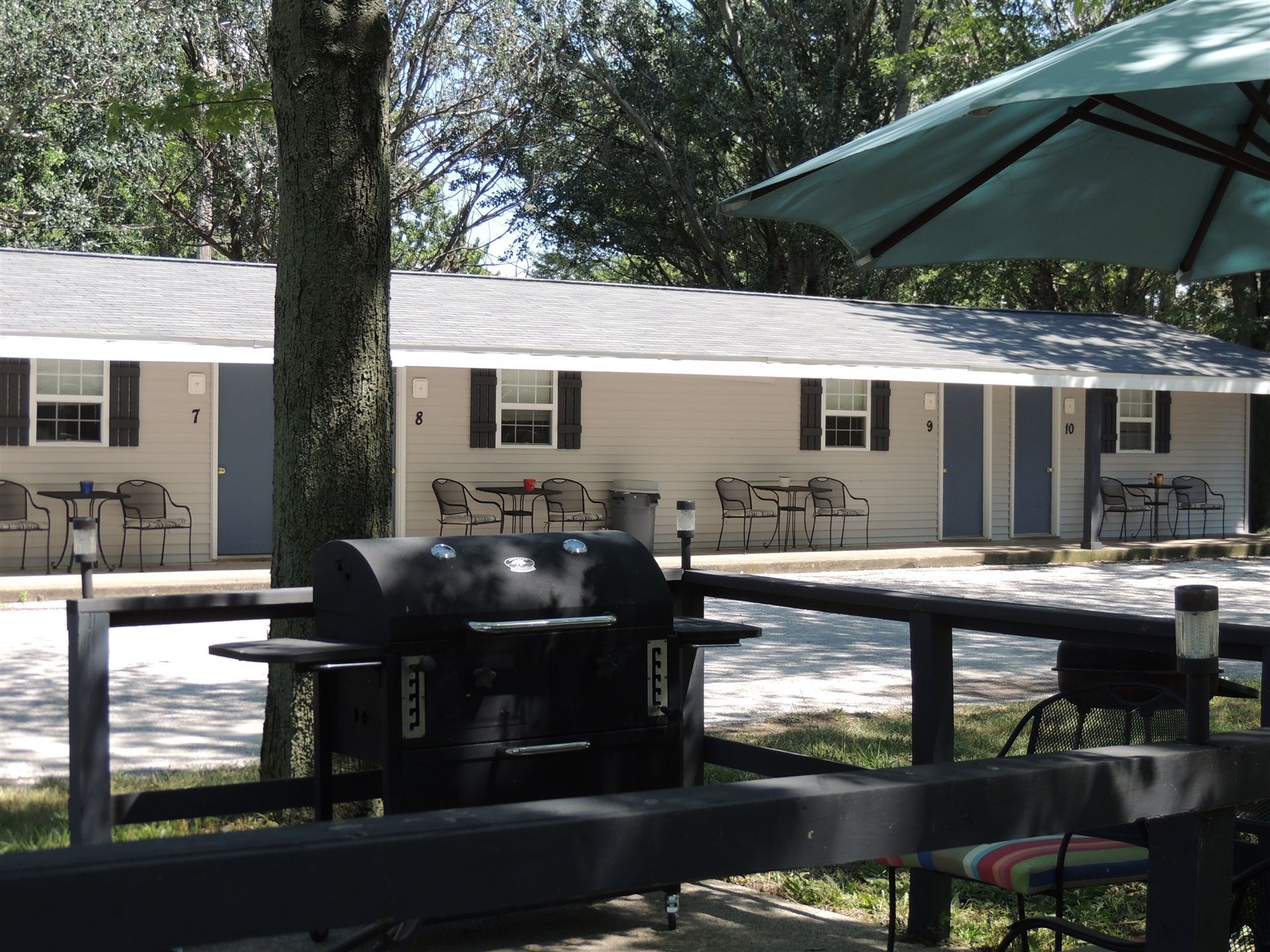 Outdoor picnic area with a grill, tables, and a beige motel-style building under trees