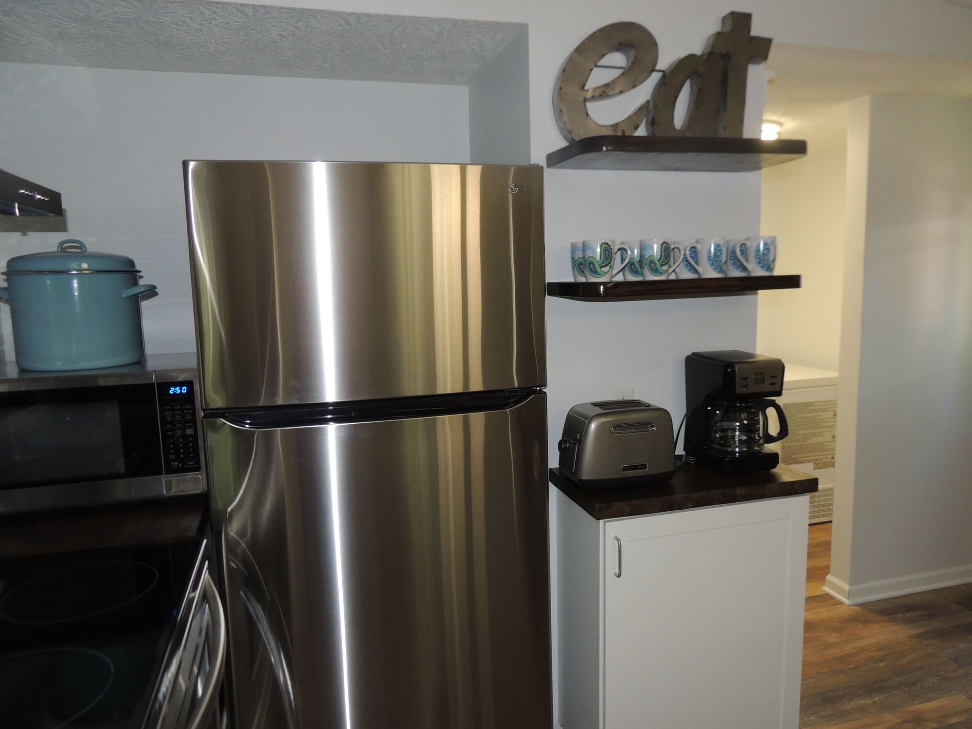 Kitchen with stainless steel refrigerator, white cabinet, shelves, and small appliances in the background
