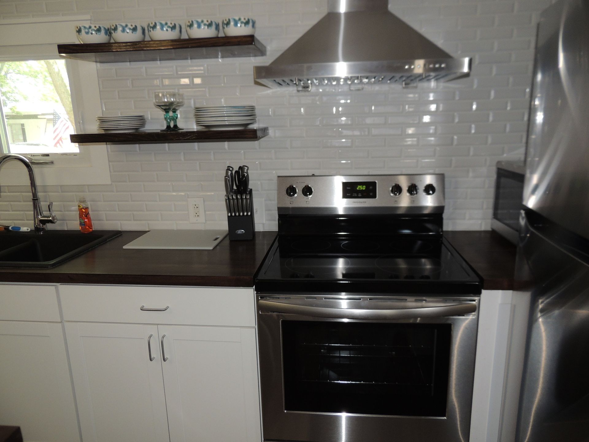 Modern kitchen with black countertops, white cabinets, stainless steel range hood, and refrigerator