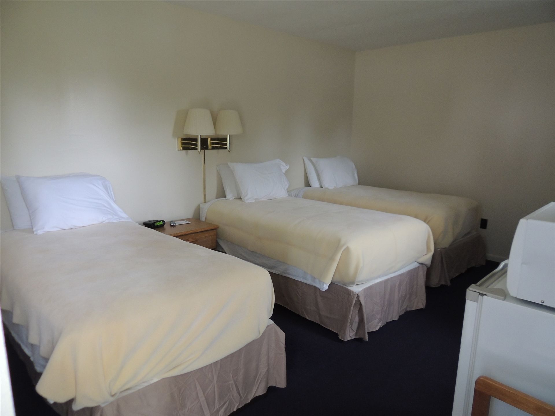 Three neatly made twin beds in a simple hotel room with beige walls and dark carpet.