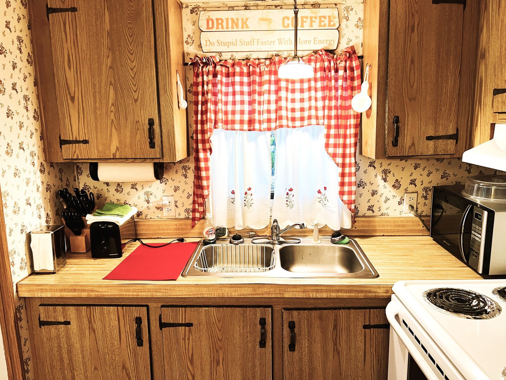 Cozy kitchen with wooden cabinets, red accents, a sink under a window, and a white stove at right