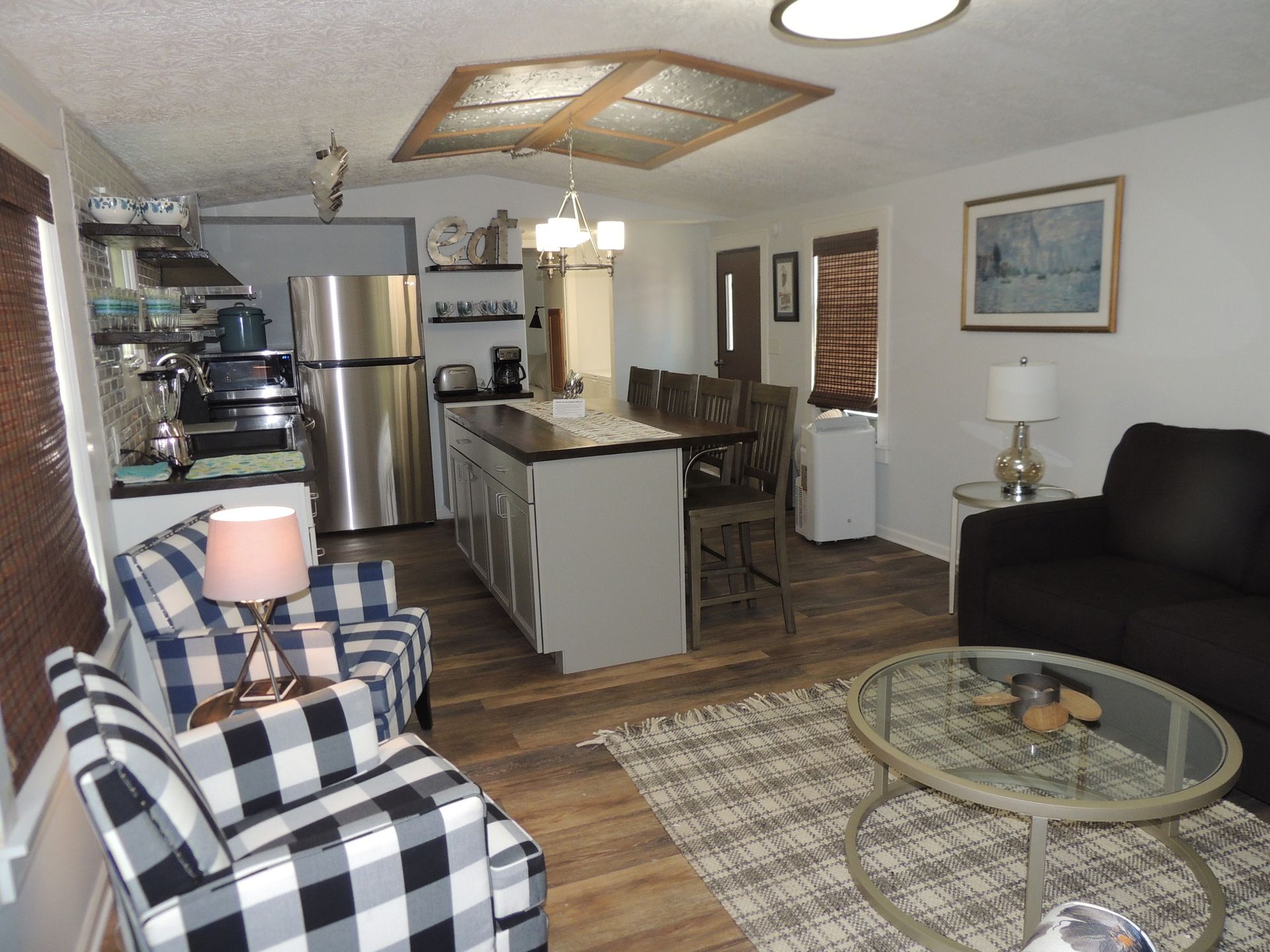 Cozy open-plan living room and kitchen with plaid chair, glass coffee table, and stainless steel appliances