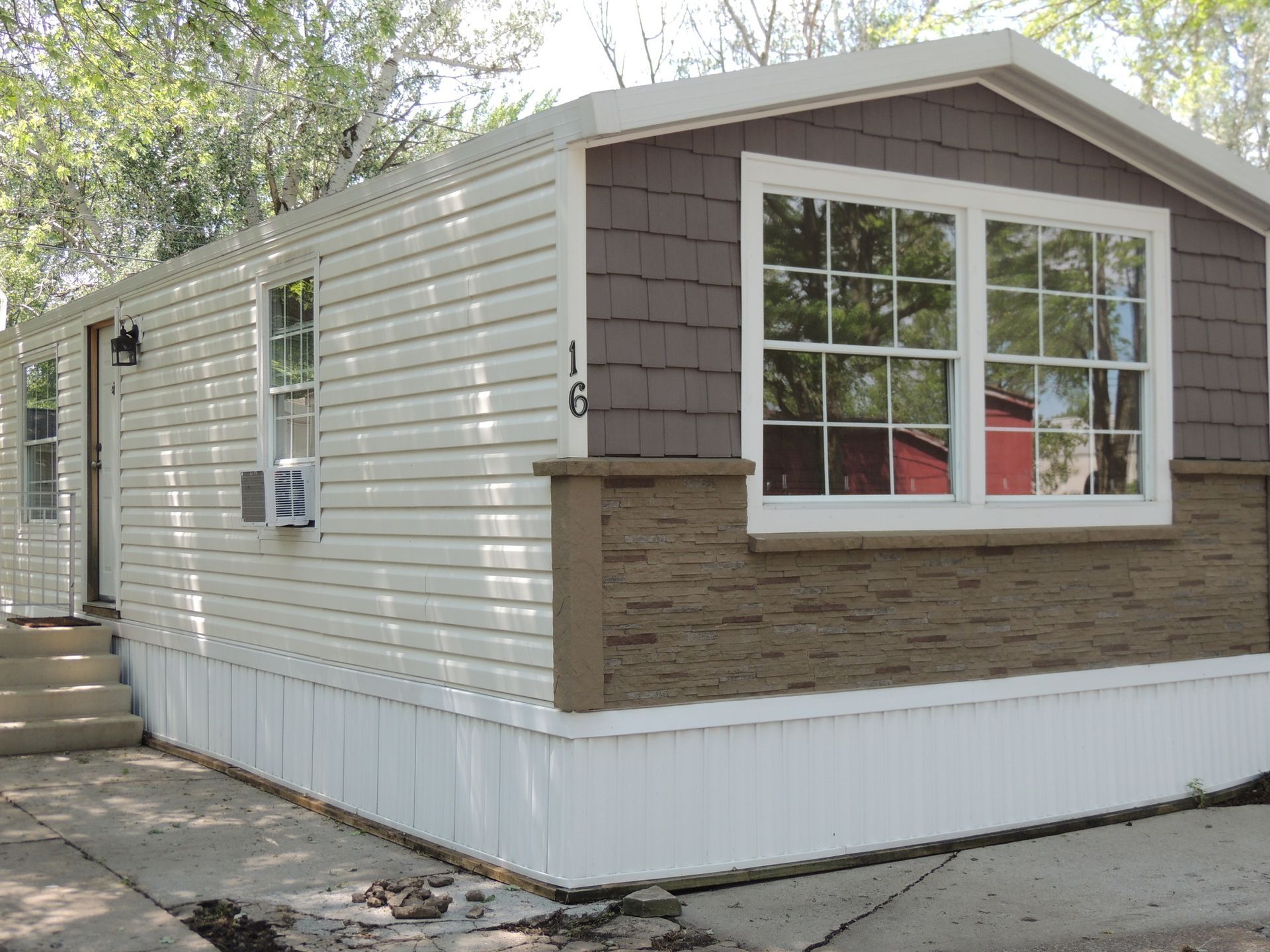 Small beige mobile home with white trim and brown stone facade, viewed from the front corner.