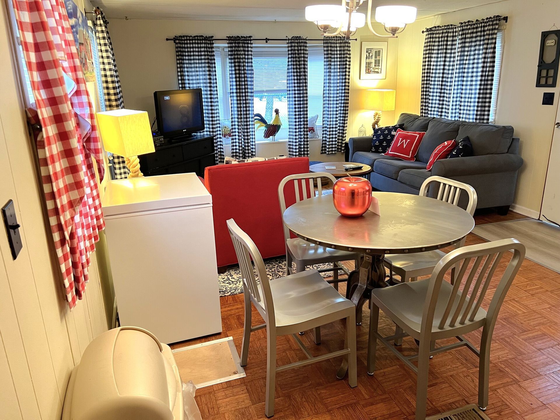 Cozy living-dining room with gray sofa, round table, red accents, TV, and patterned curtains