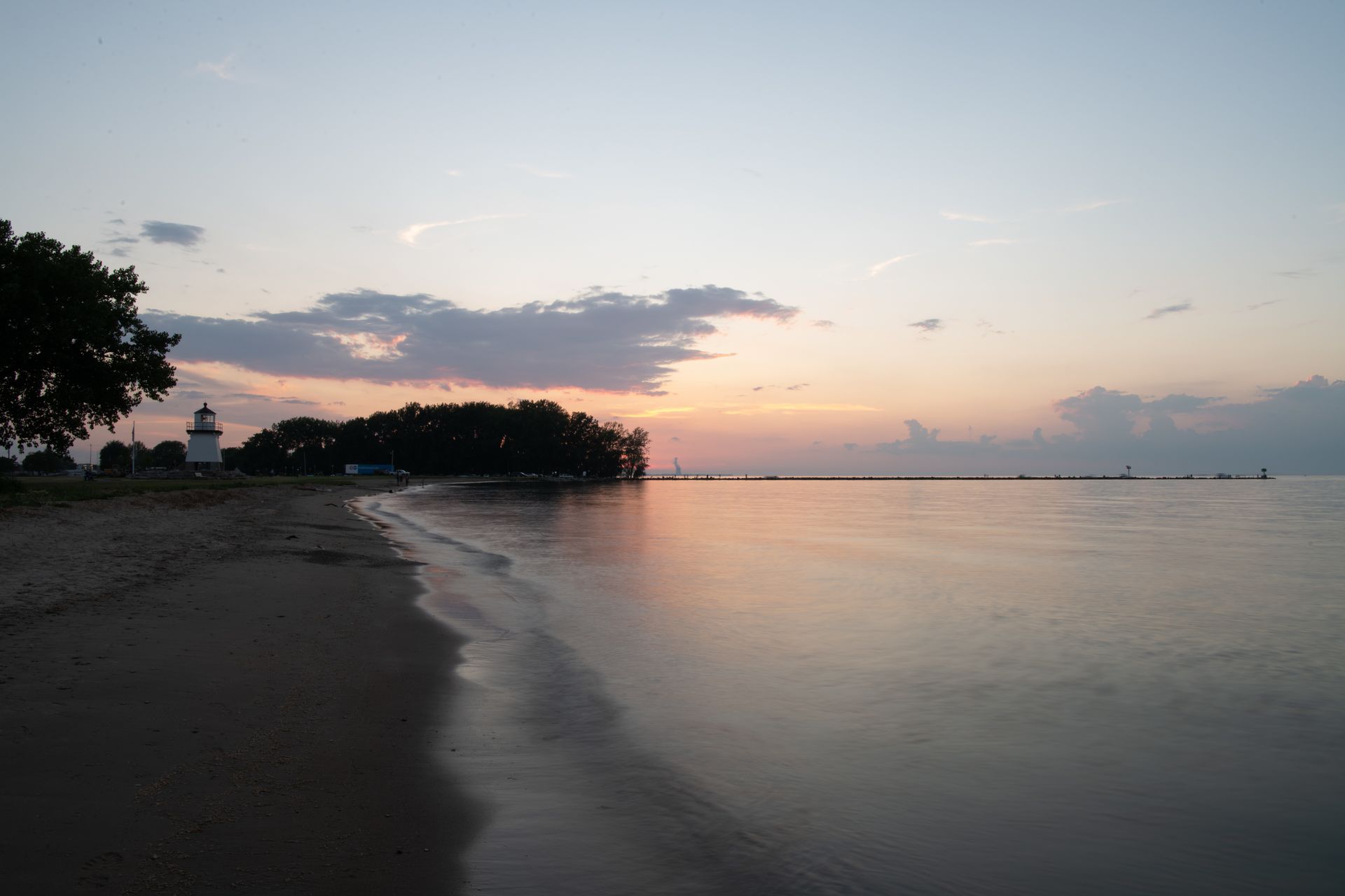 Calm beach at sunset with a dark shoreline, gentle waves, and pastel sky reflections