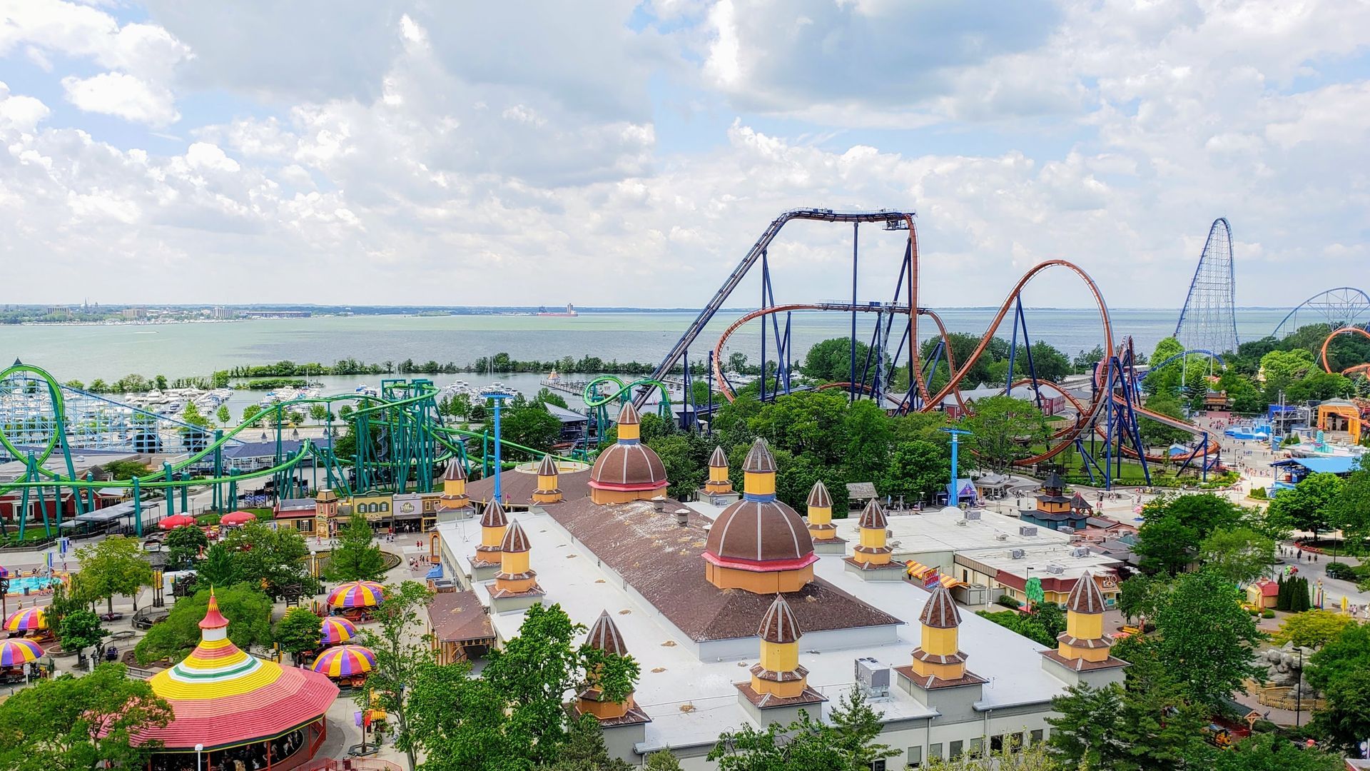 Amusement park with colorful rides, landscaped paths, and a large roller coaster under a cloudy sky