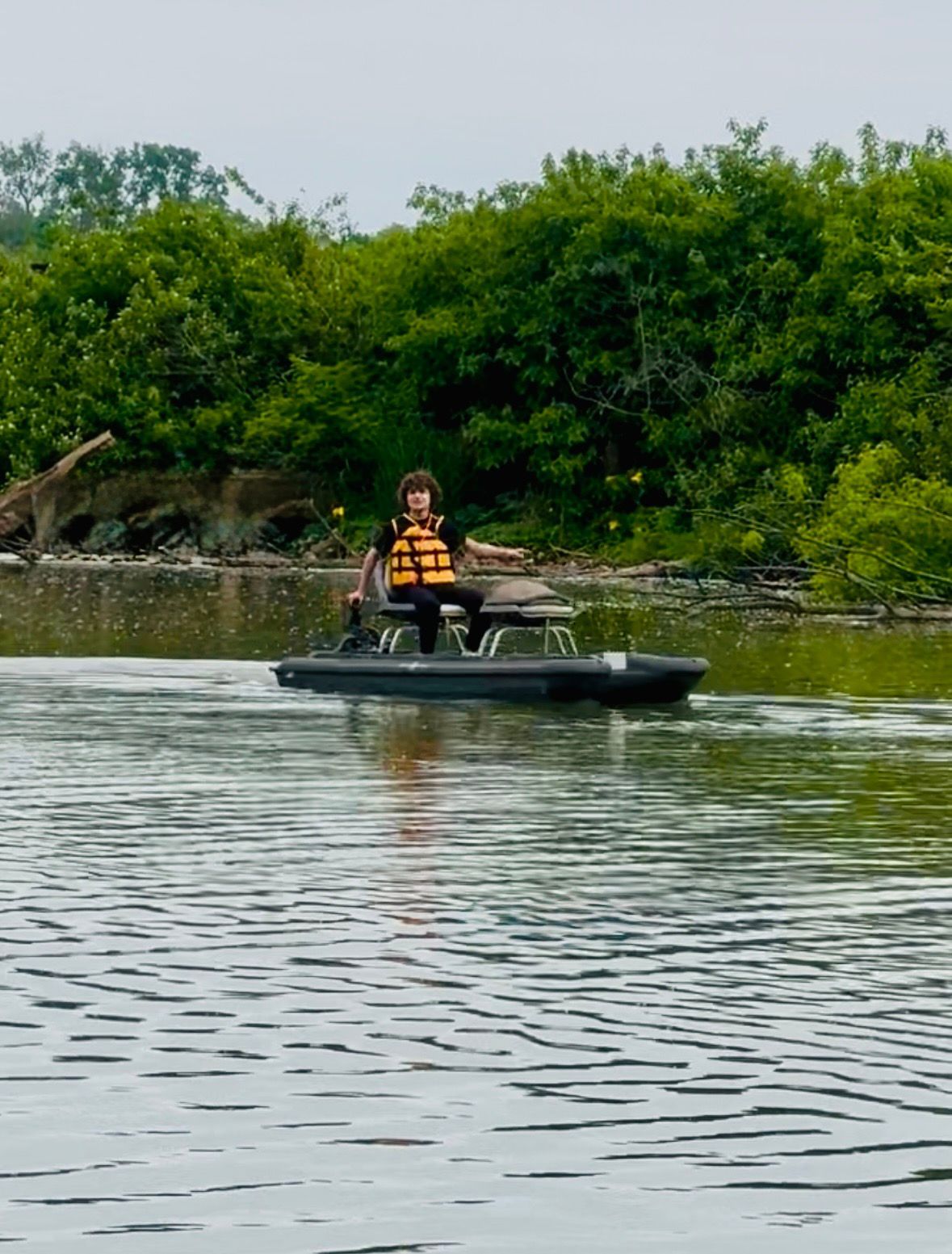Person in an orange life vest paddling a black kayak on calm water near green mangroves