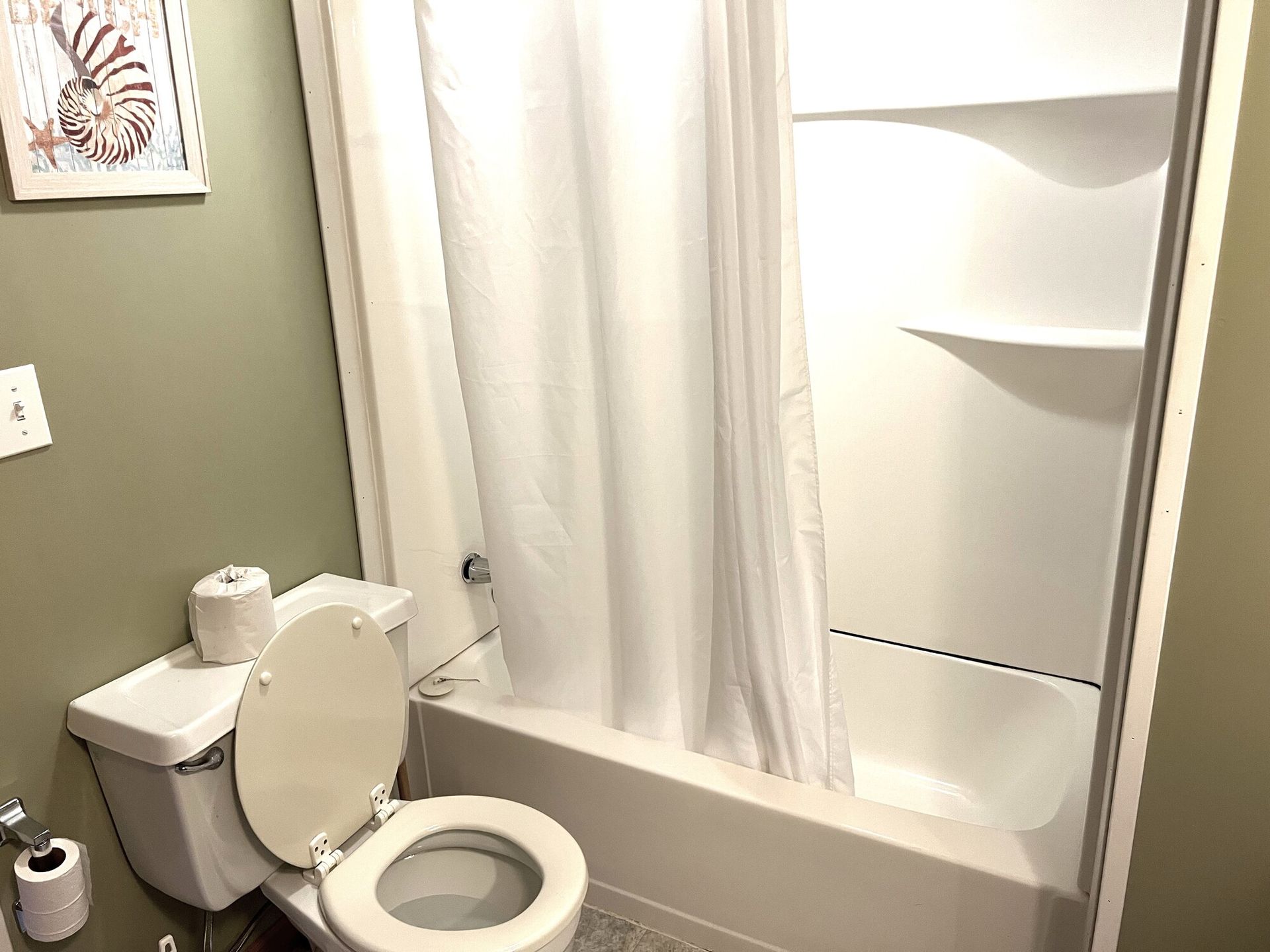 Small bathroom with a toilet, bathtub with shower curtain, and wall shelf.