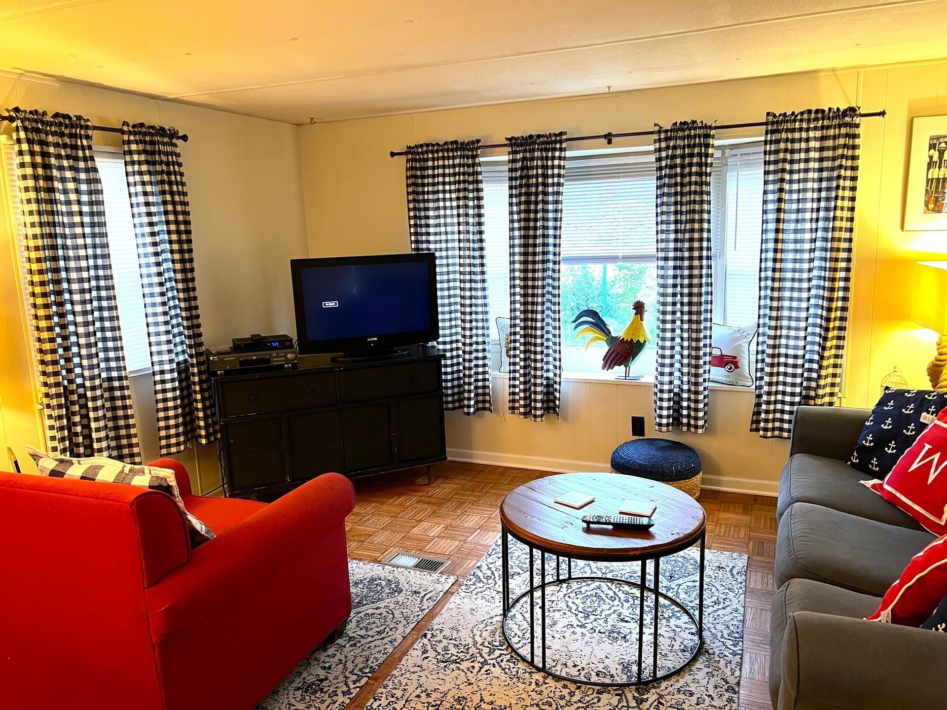 Bright living room with red sofa, gray couch, TV, coffee table, and patterned curtains.