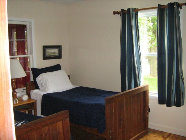 Small bedroom with a wooden bed, blue bedding, and a window with curtains.