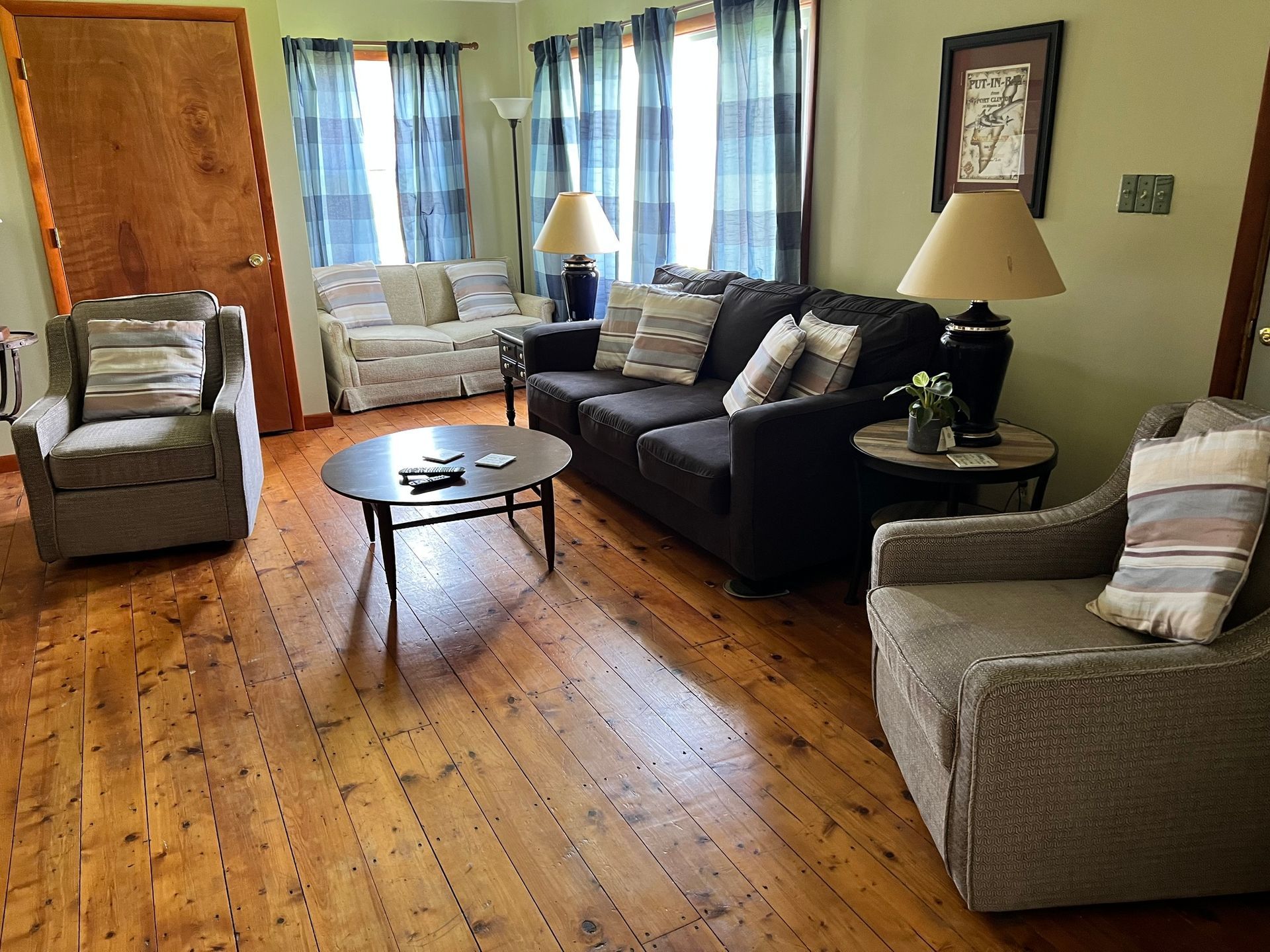 Living room with sofas, armchairs, wooden floor, coffee table, lamps, and sunlight through curtains