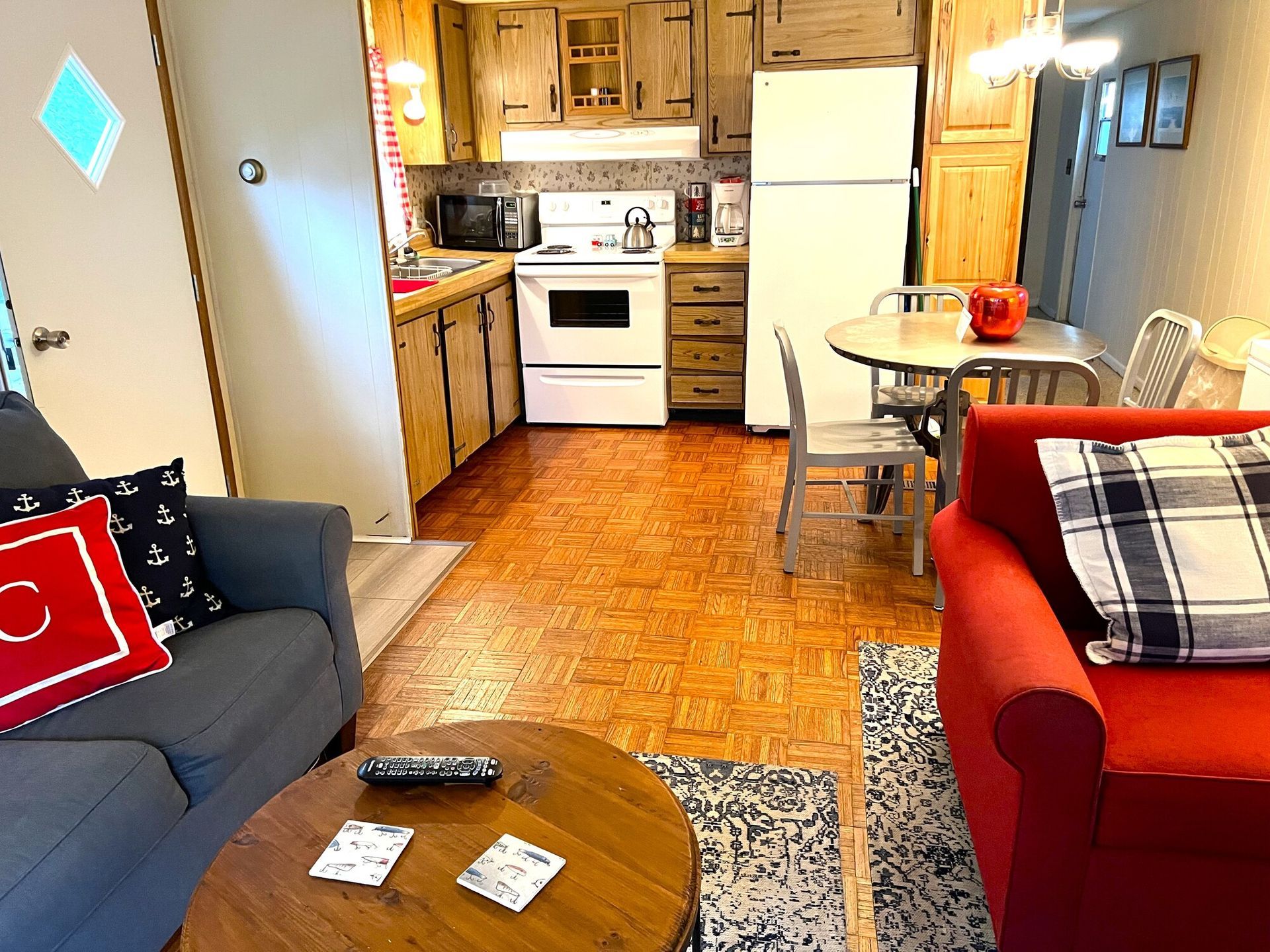 Small kitchen and dining area with red and blue couches, a round table, and a white fridge.