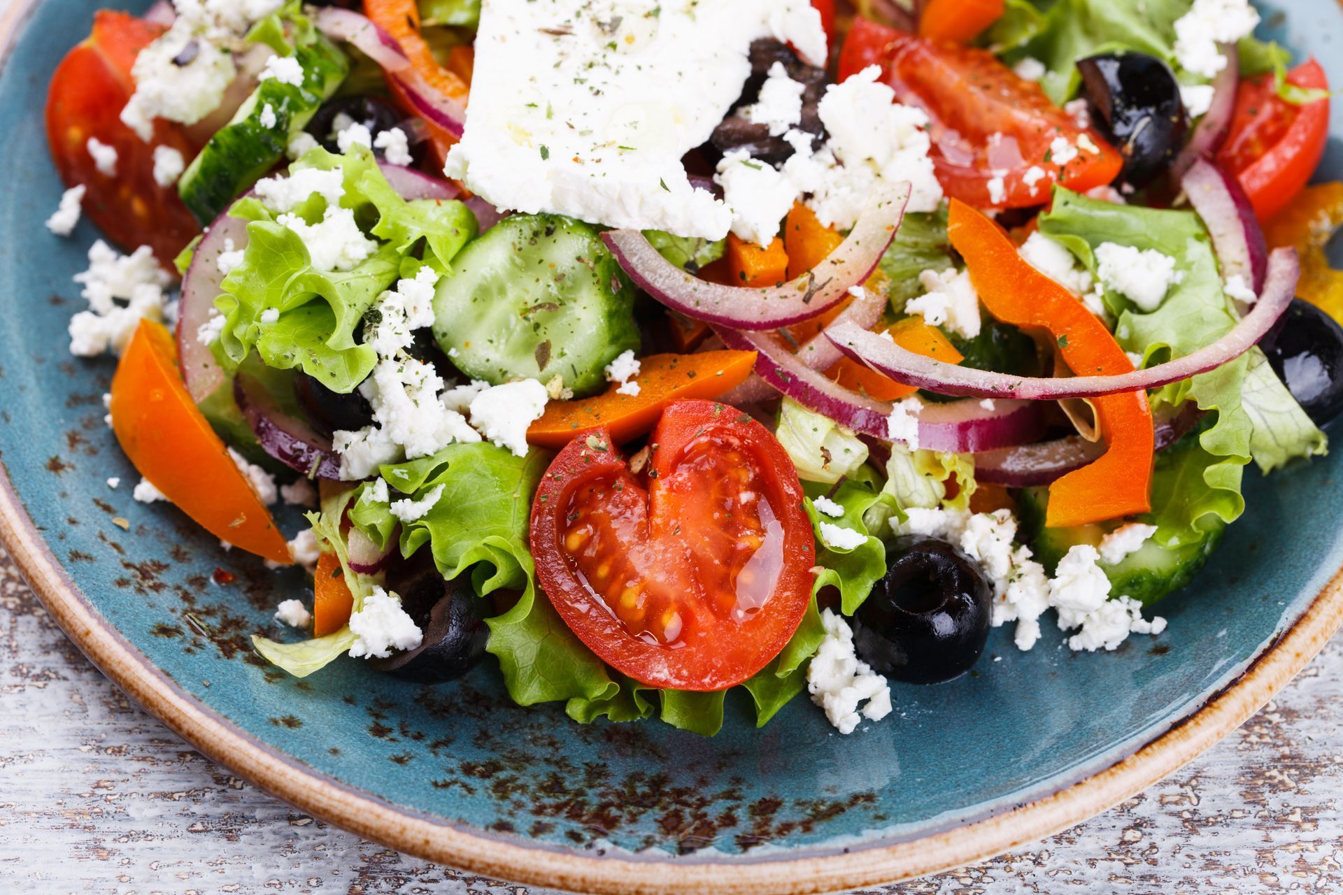 Greek salad with tomatoes, cucumbers, olives, red onions, feta, and greens on a blue plate