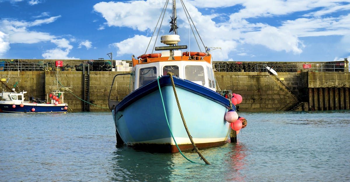 Blue fishing boat moored in calm harbor water beside a stone quay under a bright sky
