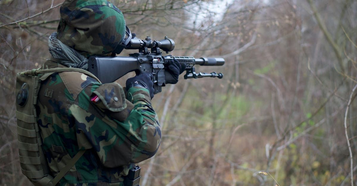 Soldier in camouflage aiming a rifle in a wooded outdoor area