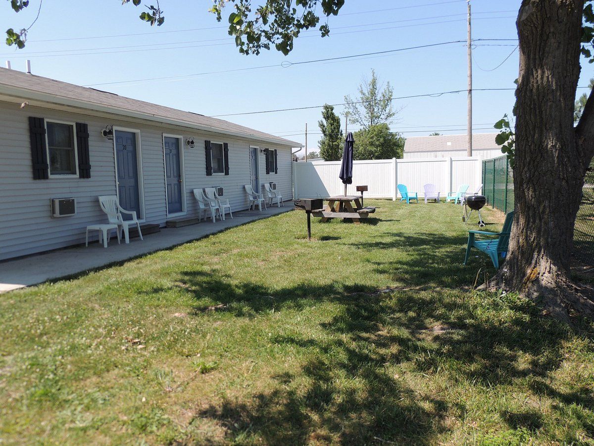 Backyard beside a white house with lawn, trees, and a patio table under a blue sky