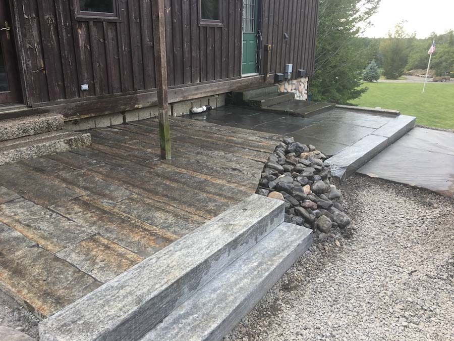 Exterior of a house with stone steps, a wooden deck, and a gravel pathway.