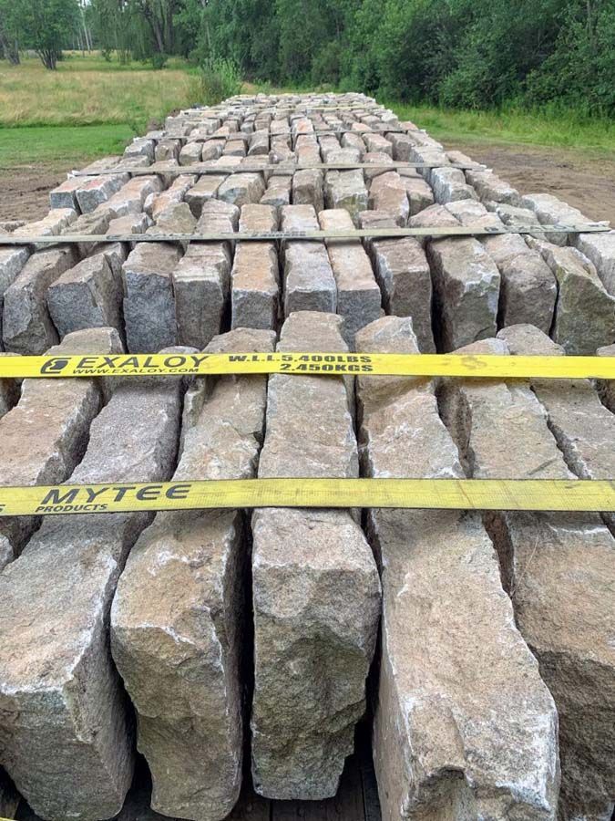 Pallet of rectangular stone blocks, secured with yellow straps, outdoors.