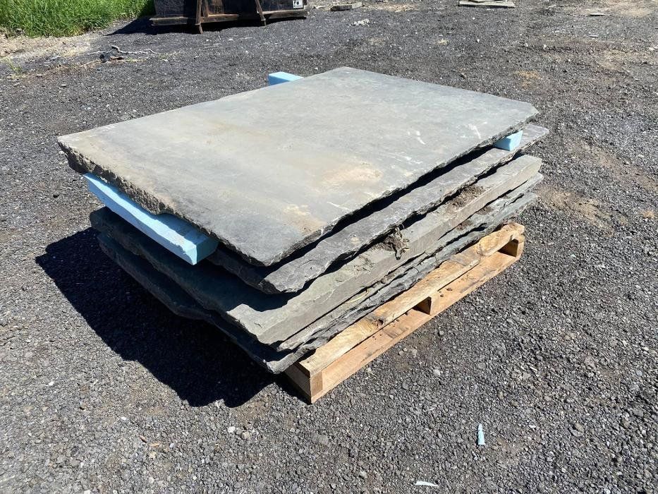 Stack of gray stone pavers on a wooden pallet, resting on gravel.