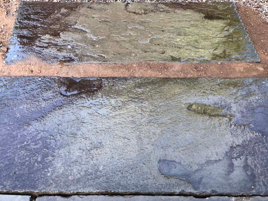 Wet, dark-colored stone slabs reflecting sunlight, laid on a reddish-brown base material.