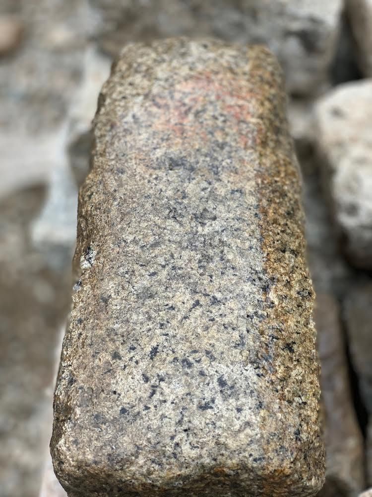 Rectangular, weathered stone with speckled gray and black coloration. Some reddish marks are visible on the top.