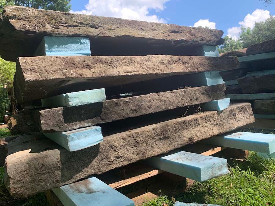 Pile of large, dark, weathered stone slabs supported by blue foam blocks outdoors.