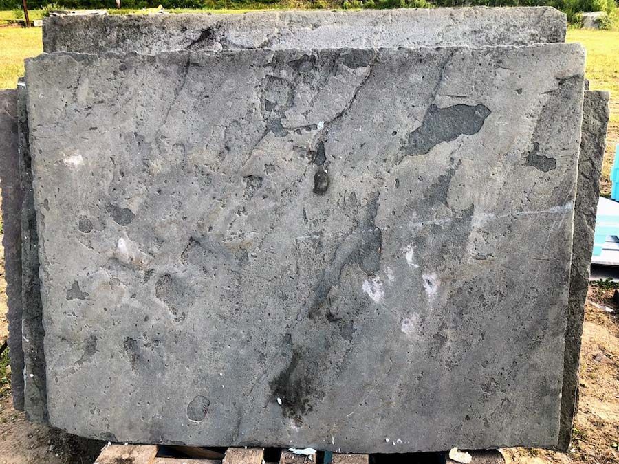 Stack of weathered, gray concrete pavers on a wooden pallet, outdoors.
