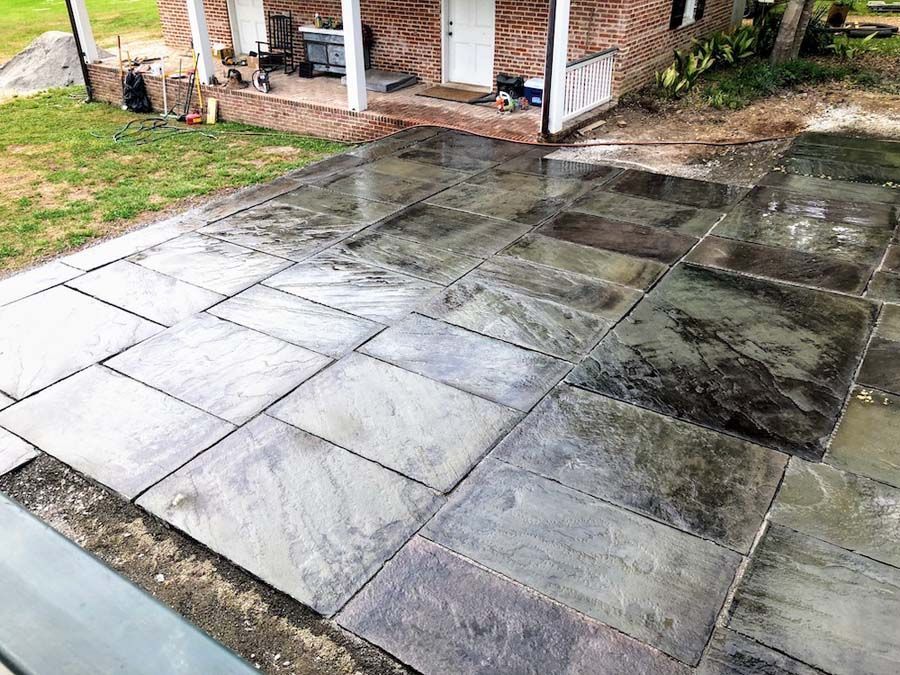 Newly installed slate patio outside a brick house. Grey-blue stone tiles cover the ground, reflecting light.