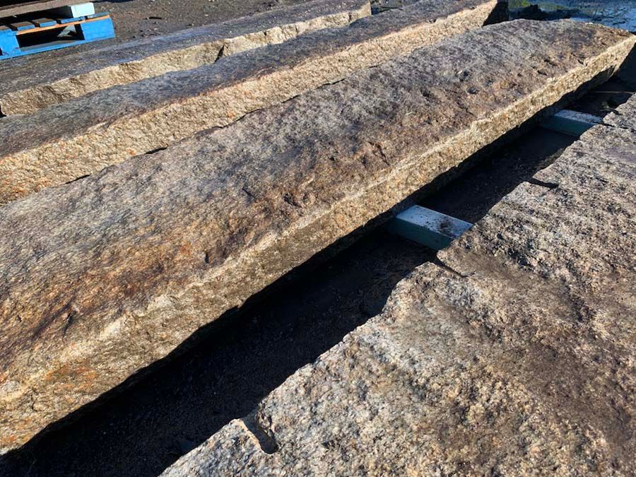 Long, rectangular, weathered stone troughs resting on supports in an outdoor setting.