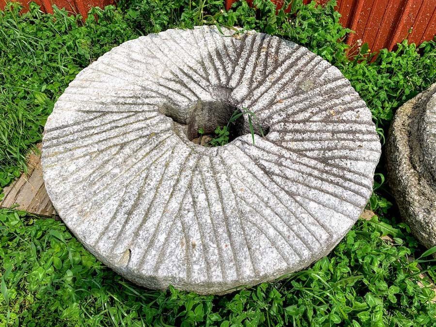 Large, circular stone millstone with carved grooves, resting in green grass.