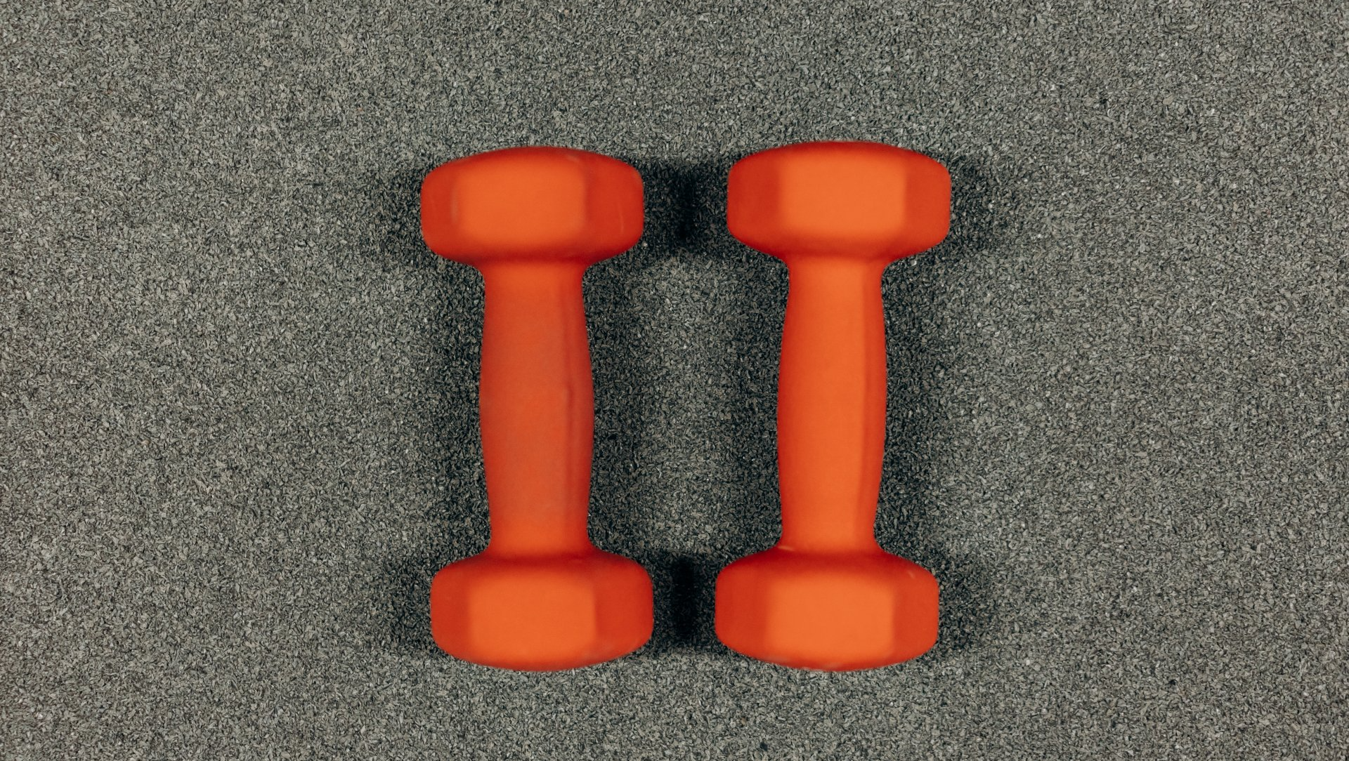 Two orange hand weights laying on grey carpet.