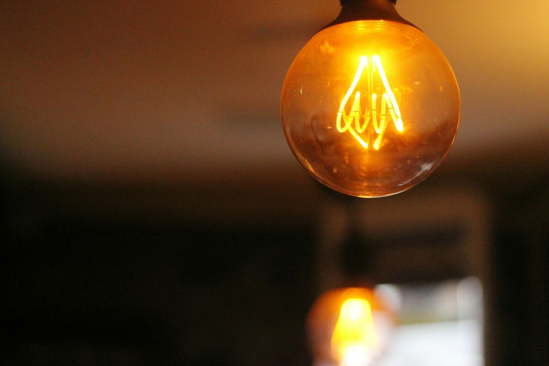 Glowing Edison-style light bulb; warm orange glow in a dimly lit setting.