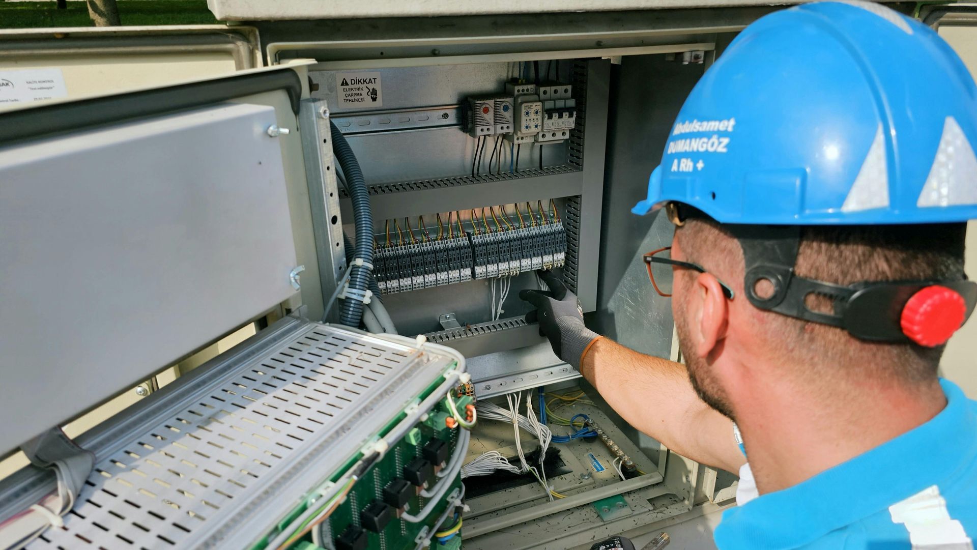 Man in blue hard hat works on electrical panel.
